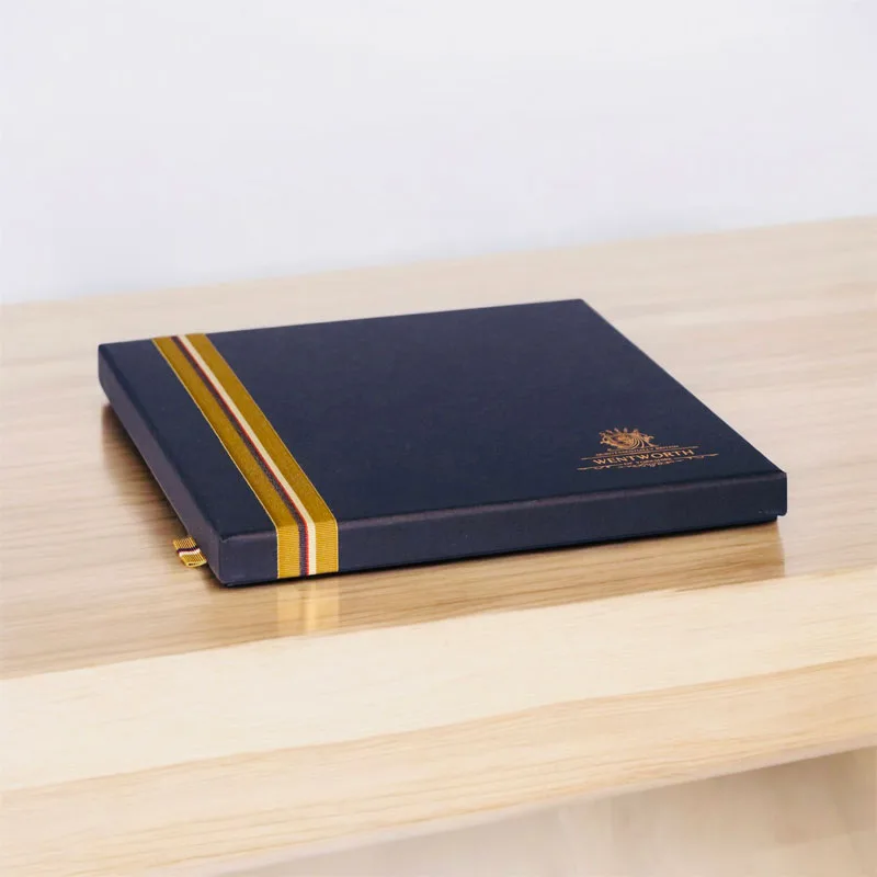 Navy rigid presentation box with a gold foil stripe on a wooden table